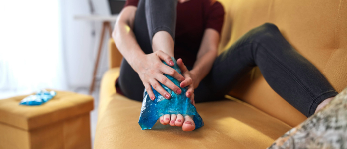 Person applying an ice pack to a swollen ankle while resting—demonstrating proper icing technique for injury recovery.