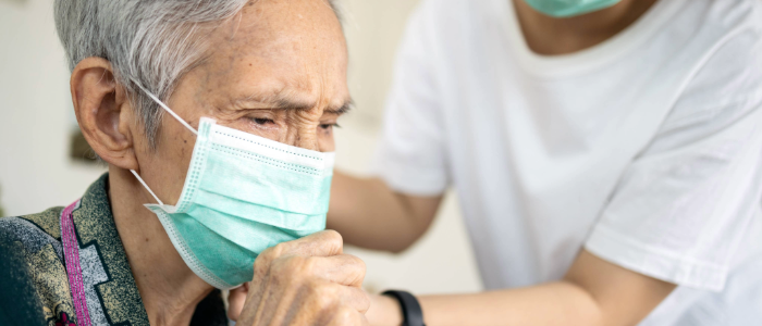 Caretaker helping an elderly woman put a mask on, so they can shop during flu season.