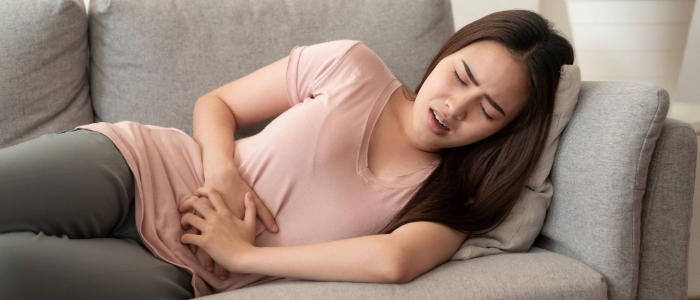 woman on the couch in severe abdominal pain after eating a meal.