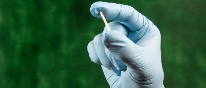 Gloved hand holding a Norplant birth control implant to demonstrate size and shape.