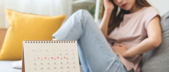 A woman holding her lower abdomen with a concerned look, possibly near a calendar (to suggest menstrual tracking)