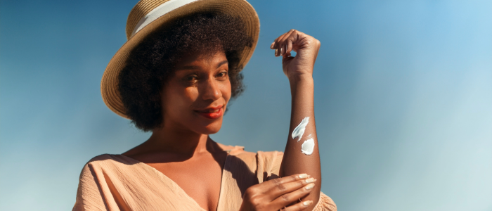 Woman with a sun rash applying sunscreen outdoors to prevent sunlight allergy symptoms.