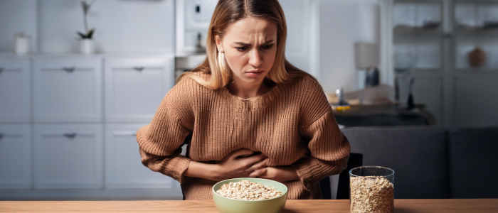 Woman experiencing stomach ulcer discomfort while sitting at table with soothing foods.